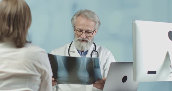 Medical doctor talking to a female patient and looking at an x-ray image in his office. 4k slow motion