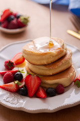 Poring honey or maple syrup on pile of homemade Japanese fluffy pancakes 