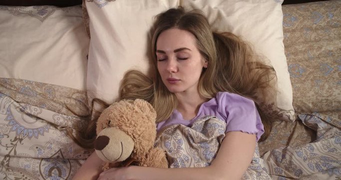 Young woman sleeping in bed hugging teddy bear