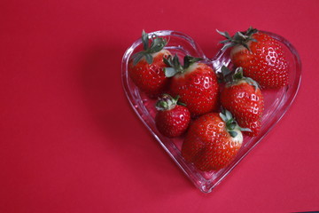 Strawberries in a hearth shaped plate with red background 