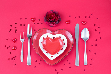 heart shaped plates, cutlery, flower and red hearts on a red background  