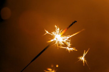 Burning sparking stick starlight fireworks pyrotechnic dark black warm background.