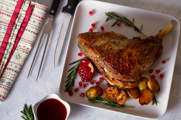 Overhead view of roast leg of lamb served with potatoes, pomegranate seeds and rosemary on white...
