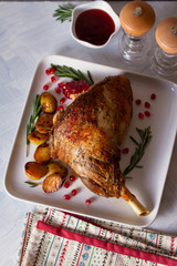 Overhead view of roast leg of lamb served with potatoes, pomegranate seeds and rosemary on white plate, flatlay