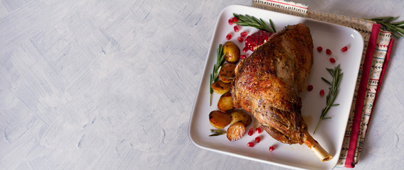 Overhead view of roast leg of lamb served with potatoes, pomegranate seeds and rosemary on white plate, copy space, flatlay © freeskyline