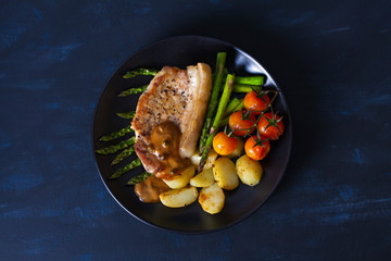 Roast pork chop with pepper sauce, asparagus, potatoes and tomatoes. View from above, top view