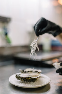 Chef of the restaurant add some sliced onions to oysters with caviar, leeks and tiger milk sauce. Blurred background of restaurants kitchen. Smooth image with shallow depth of field.