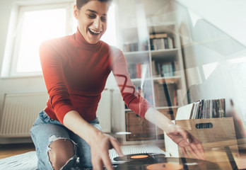 Smiling woman playing favorite vinyl record on turntable