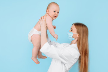 A young female pediatrician, holding a child in her arms, makes an examination of the child on an isolated blue background