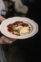 Waitress holding beef steak with potatoes gratin and green sauce on a plate. Smooth image with shallow depth of field.