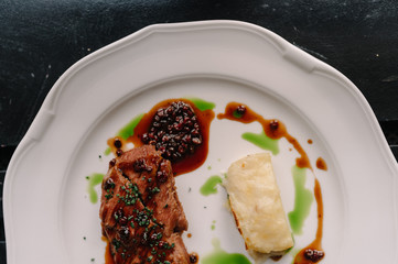 Beef steak with potatoes gratin and green sauce on a plate. Dark background. Smooth image with shallow depth of field.