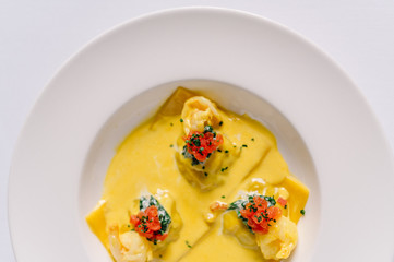 Plate of raviolli pasta with shrimps, salmon and curry sauce. Light background. Smooth image with shallow depth of field. Top close up view.