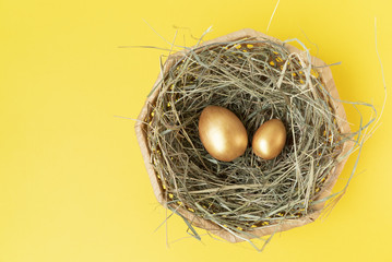 Golden eggs in the wicker basket with hay on the yellow background.Happy Easter. Top view. Flat lay. Copy space. Place for text and design.