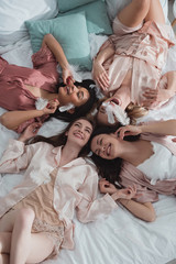 Obraz na płótnie Canvas Top view of happy and excited multiethnic women resting on bed with feathers at bachelorette party