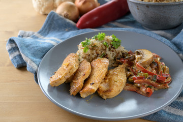 Healthy meal with chicken filet, cauliflower rice, bell peppers and mushroom on a blue plate on a wooden table