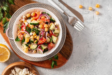 Chickpea salad with tomatoes, cucumber, feta cheese, parsley, onions and lemon in a plate on a concrete background top view, copy space. Healthy vegetarian food, oriental and Mediterranean cuisine.