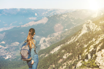 Obraz premium Young beautiful girl travels alone in the mountains in spring or autumn, looks into the distance and enjoys nature, rocks and green forests, view of the landscape. a backpack behind and sportswear