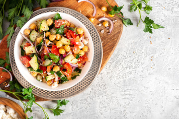 Chickpea salad with tomatoes, cucumber, feta cheese, parsley, onions and lemon in a plate on a concrete background top view, copy space. Healthy vegetarian food, oriental and Mediterranean cuisine.