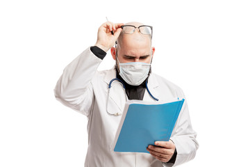 A male doctor in a mask looks at the documents. A busy schedule during the coronavirus pandemic. Isolated on a white background.