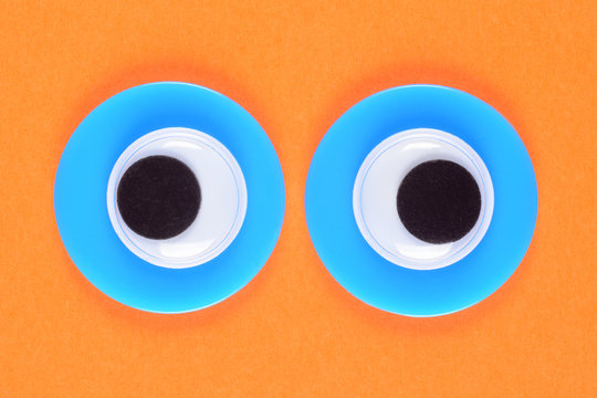 Googly toy eyes. Neon green mad strabismus eyes look straight at you, on a background of orange paper. Macro close-up.