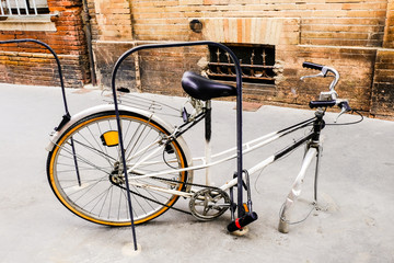 Bicycle with a stolen front wheel is chained to a bicycle parking lot.