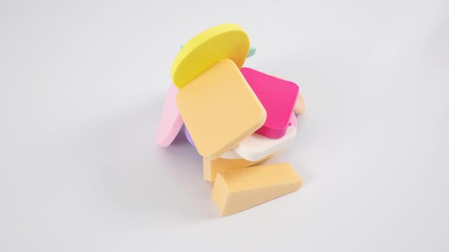  Abstract composition of colored cosmetic sponges, white background. Dolly shooting.