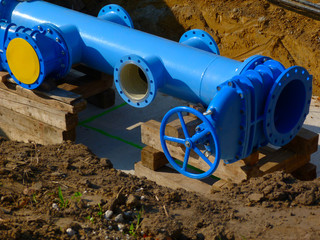 Fototapeta na wymiar large diameter painted blue steel water main pipe installation. excavated trench. closing valve, connections, bolts, coupling rims. yellow plastic cap. infrastructure.