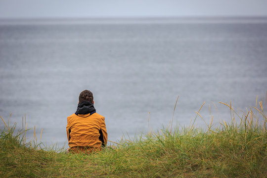 Lonely and melancholy person looking at the sea from the back on a desolated coast of iceland