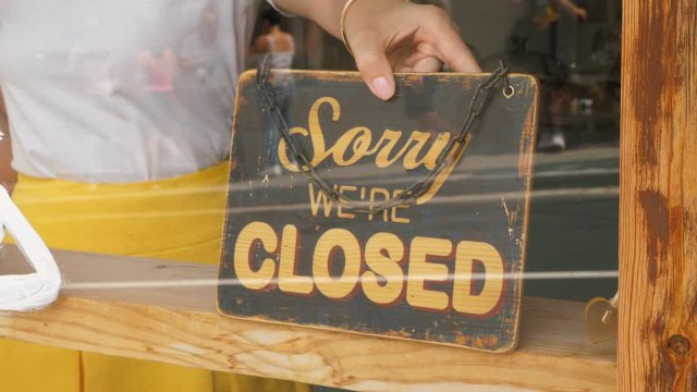 Owner woman set 'closed' sign at window of small shop, indicate break for lunch time or end of workday. Closeup shot of vintage sign plate stick behind window glass