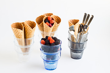 Conical,Crispy Ice Cream Cornets on the white surface with jelly berries,glass ice cream cups and spoons.