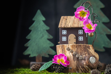 Miniature cozy wooden toy house cottage with pink flowers on moss background, spring Easter postcard concept