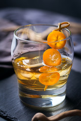 Glass of strong alcohol, whiskey, ice, kumquat on a table