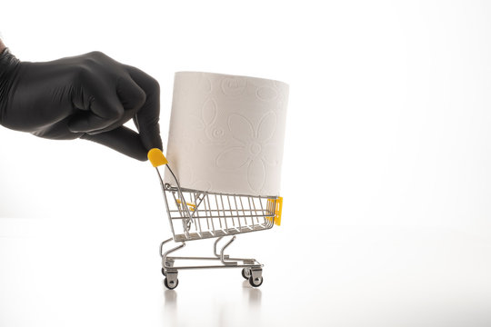 Consumer buying panic about coronavirus covid-19 concept. Toilet paper roll in shopping trolley.A black gloved hand is driving trolley for hygiene.People are stocking up essentials for home quarantine