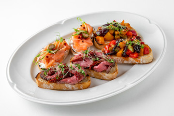 Bruschetta with salmon, capers, grilled vegetables and pork or beef slices. Banquet festive dishes. Gourmet restaurant menu. White background.