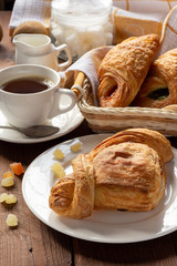 A variety of puff pastry buns with cherries, kiwi, apricot. Rolls, croissants with various fillings. A Cup of coffee with milk, Breakfast. Still-life.