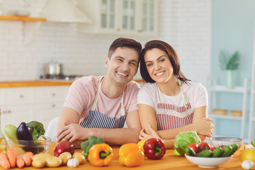 Happy middle couple smiling at a table with fresh vegetables make salad in the kitchen.