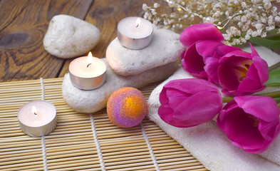 Fototapeta na wymiar Romantic spa with bath bomb, tulips, candles and pebbles on wooden background. Resort concept for Valentines day, Mothers day or wedding greeting card.