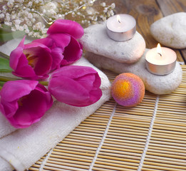 Romantic spa with bath bomb, tulips, candles and pebbles on wooden background.  Resort concept for Valentines day, Mothers day or wedding greeting card.