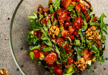 Vegetable salad with arugula, tomatoes, avocado, splashed with balsamic sauce in a glass bowl