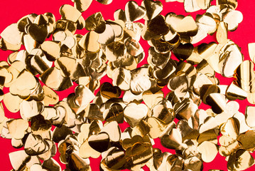 Golden candy in the form of small hearts on a bright red background.