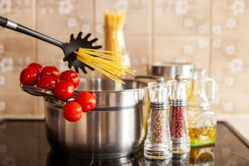 Spaghetti in a pan on a vitro-ceramic hob with tomatoes and spices