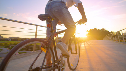 Fototapeta na wymiar LENS FLARE: Unrecognizable man in a hurry rides his bike across an overpass.