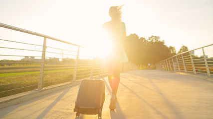 LENS FLARE: Female traveler in high heels walks across bridge and to the airport