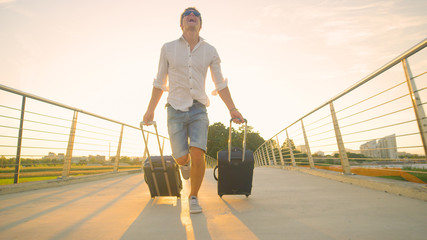 LOW ANGLE: Male tourist late to airport runs across an overpass with luggage - obrazy, fototapety, plakaty