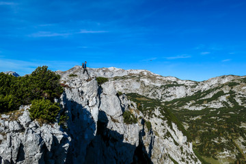 A man with a hiking backpack standing at the mountain ledge in Hochschwab region in Austria. There are many mountain ranges around her. The slopes overgrown with mountain pine, partially barren rocks