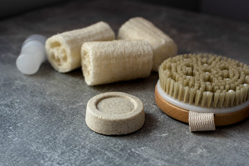 eco brush, crystal deodorant,luffa, solid shampoo on grey background. Flat lay on eco cosmetics....