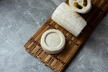 Beige solid soap bars or shampoo and loofah on wooden stand grey background. Eco bathroom...