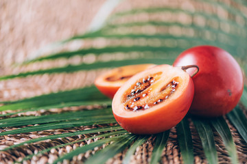 Tamarillo fruit or terong belanda with palm leaves on rattan background. Copy space. Tropical...