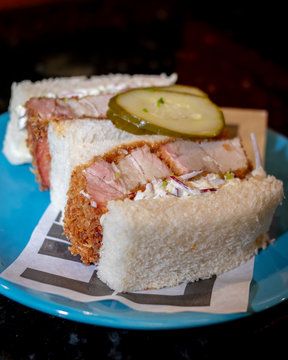 P&atilde;o recheado com barriga de porco e salada de repolho com picles dentro de um prato azul em fundo escuro de marmore  Katsu Sando de Barriga Suina  Salada Coleslaw  molho chuno 