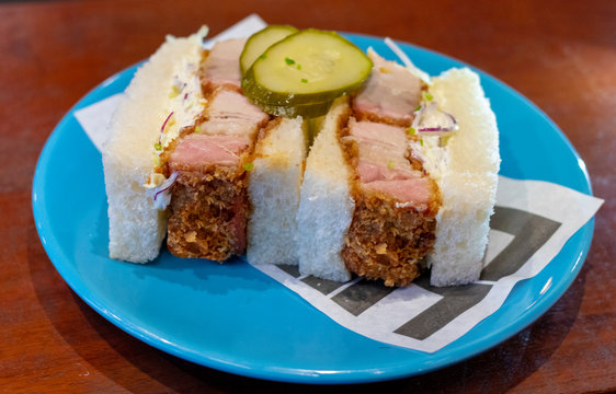 P&atilde;o recheado com barriga de porco e salada de repolho com picles dentro de um prato azul em fundo escuro de marmore,  Katsu Sando de Barriga Suina  Salada Coleslaw  molho chuno 